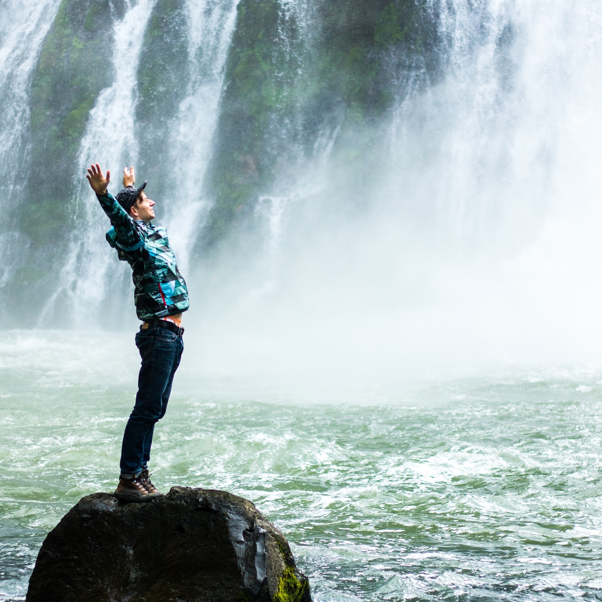 man standing on black rock surrounded body of water